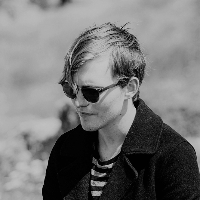 Black and white photo of a blonde man in a black jacket and sunglasses.